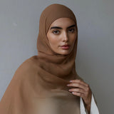 Woman wearing a brown hijab against a plain background