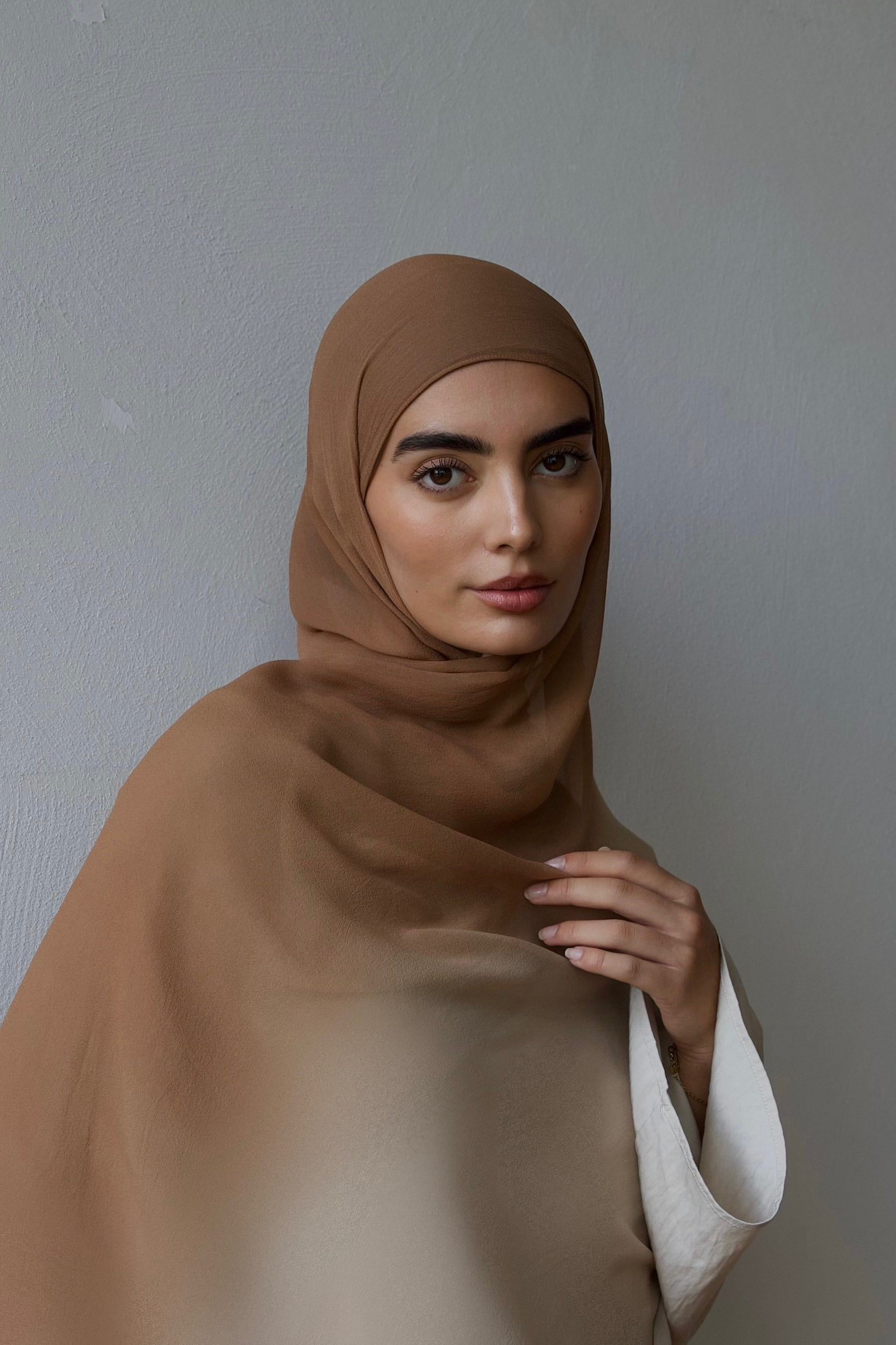 Woman wearing a brown hijab against a plain background