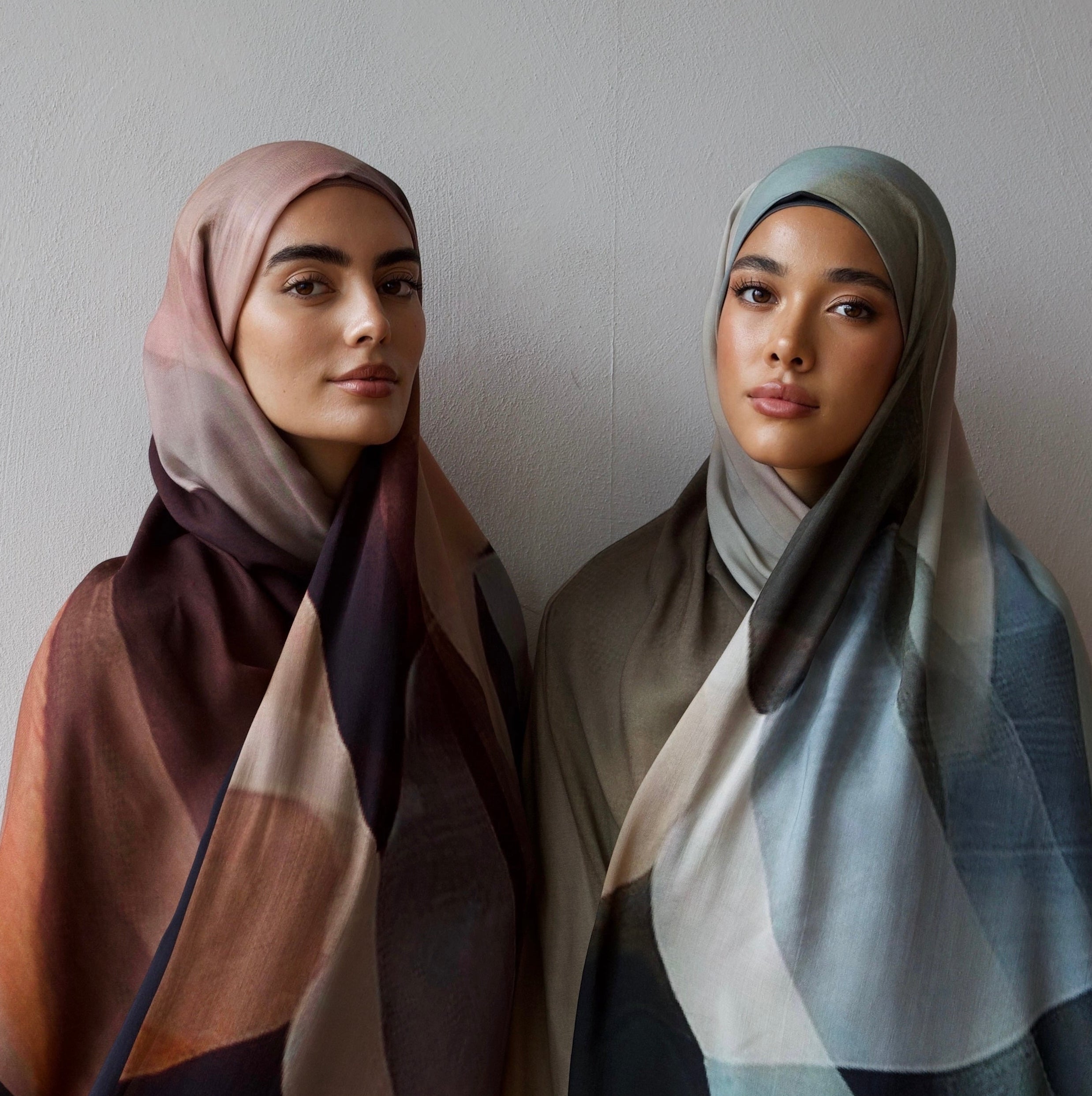 Two women wearing patterned hijabs against a plain background