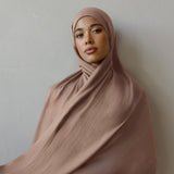 Woman wearing a flowing brown hijab against a plain background