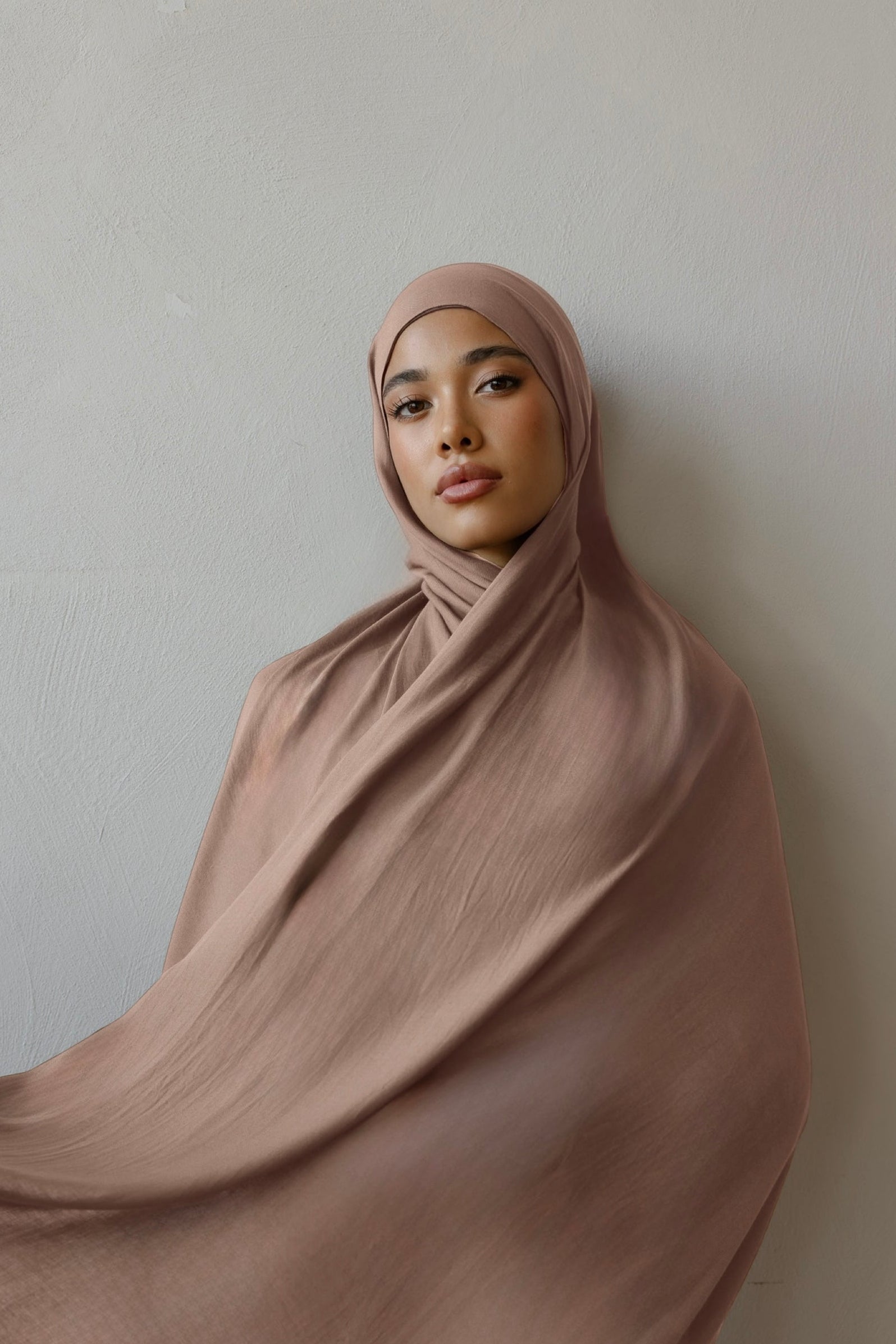 Woman wearing a flowing brown hijab against a plain background