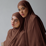 Two women wearing brown hijabs sitting on a gray background