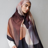 Woman wearing a patterned hijab and white dress against a plain background