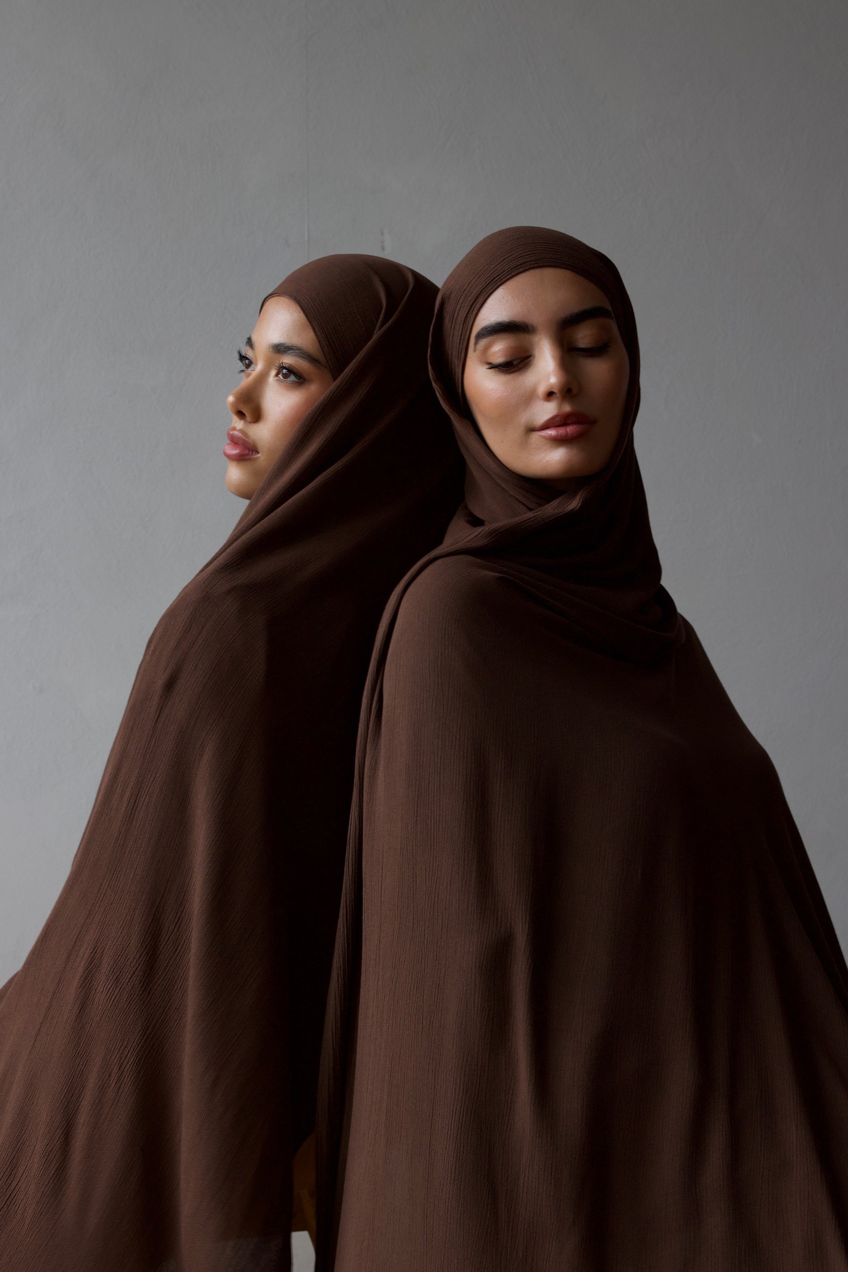 Two women wearing brown hijabs against a gray background