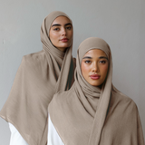 Two women wearing beige hijabs and white clothing against a plain background