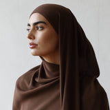 Woman wearing a brown hijab and white outfit against a plain background