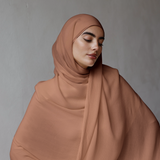 Woman wearing a brown hijab against a gray background