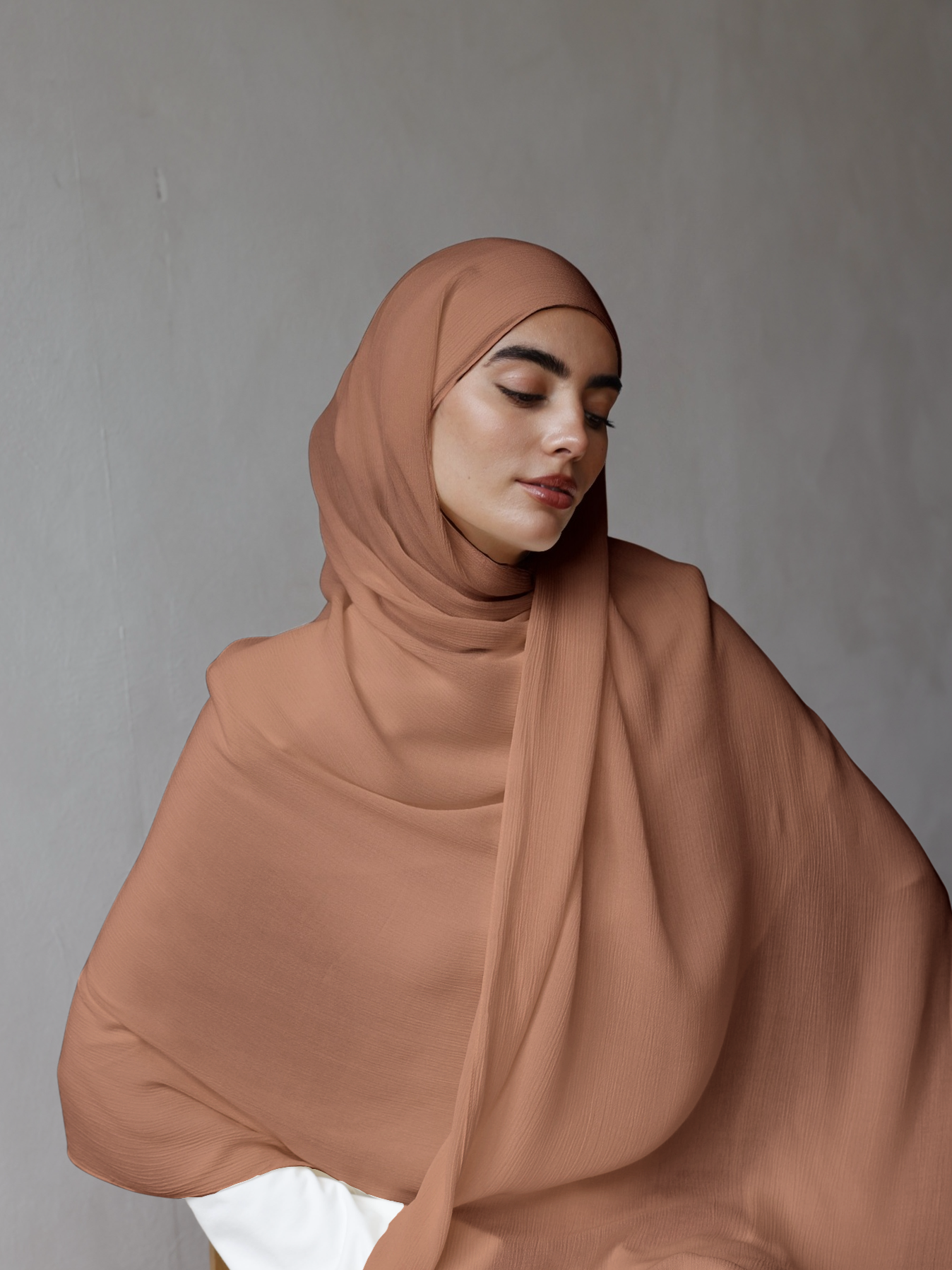 Woman wearing a brown hijab against a gray background